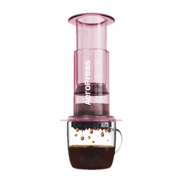 Zdjęcie różowego zaparzacza AeroPress Clear Pink, umieszczonego na szklance z zaparzaną kawą. Widoczna jest ekstrakcja kawy, której krople spadają do kubka, ukazując proces parzenia kawy metodą AeroPress.