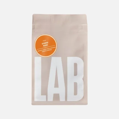 Beżowe opakowanie kawy Coffeelab z dużym napisem „LAB” i okrągłą pomarańczową etykietą z napisem „Etiopia Rudo, filtr”. Na etykiecie znajdują się nuty smakowe: czerwone owoce, trawa cytrynowa, mleczna czekolada.